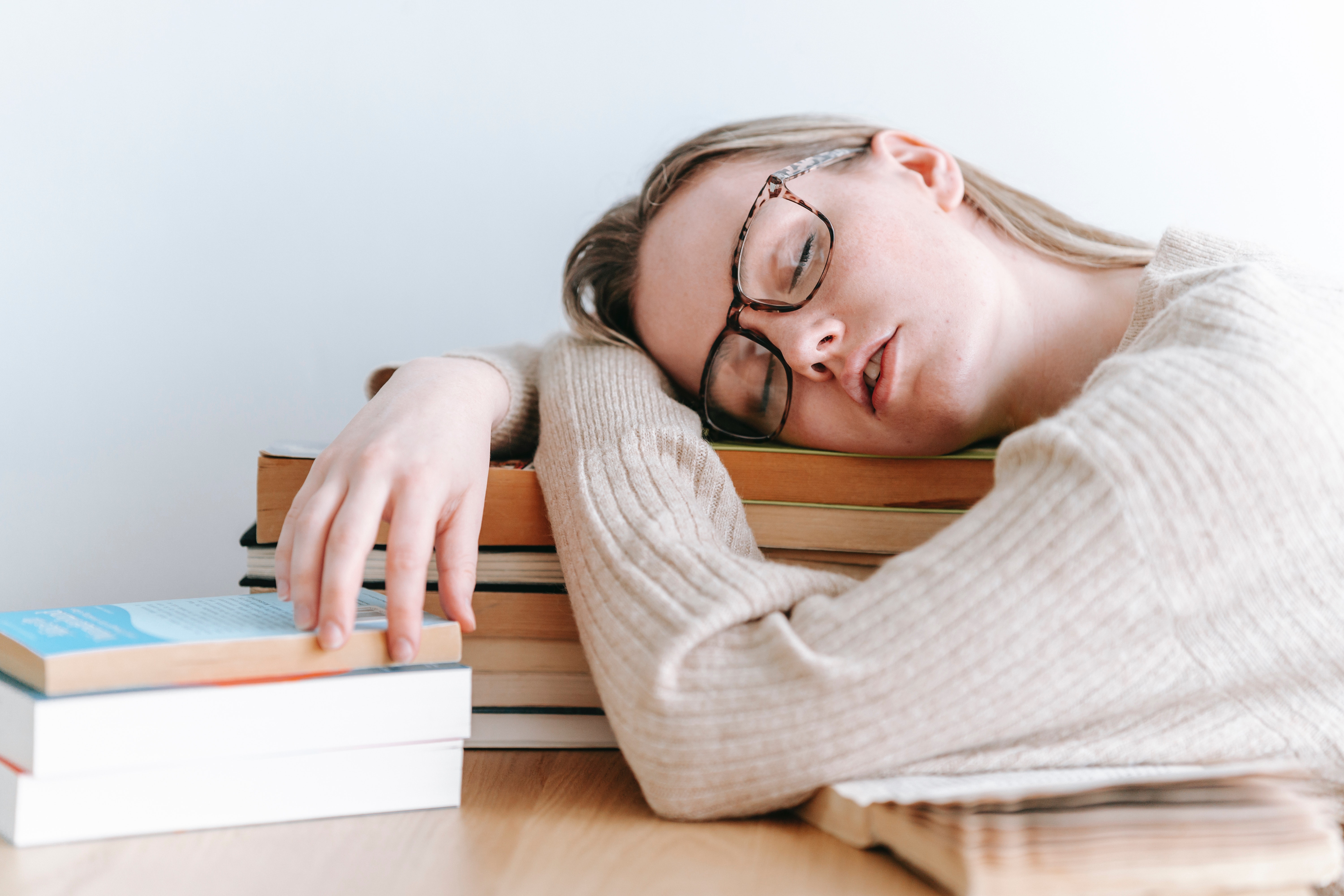 Une femme qui dort sur son bureau, elle semble épuisée par le travail. Son bureau est en désordre. 